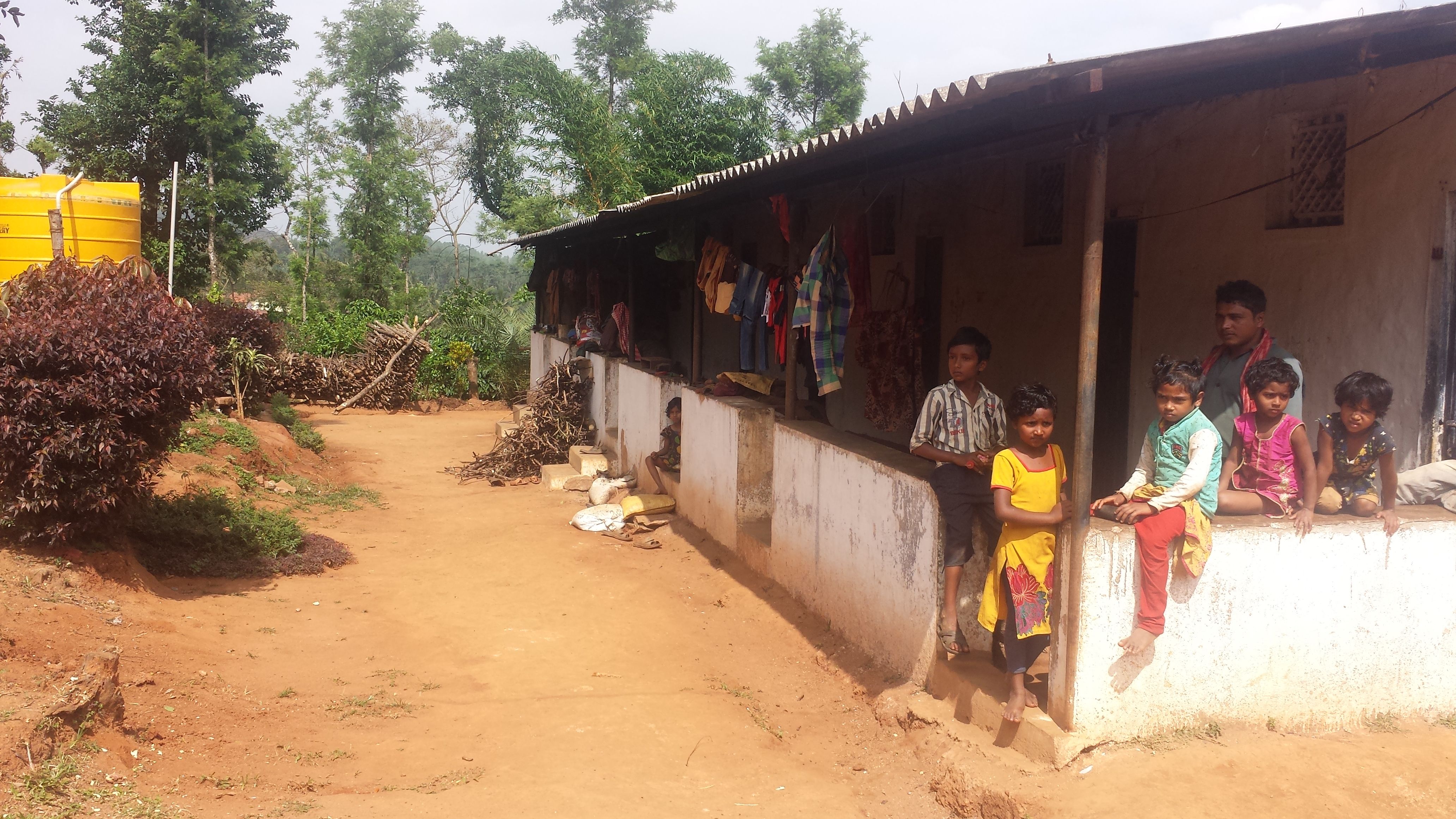 Niñas, niños y un joven sentados en el corredor de viviendas de trabajadores en una finca de café en India